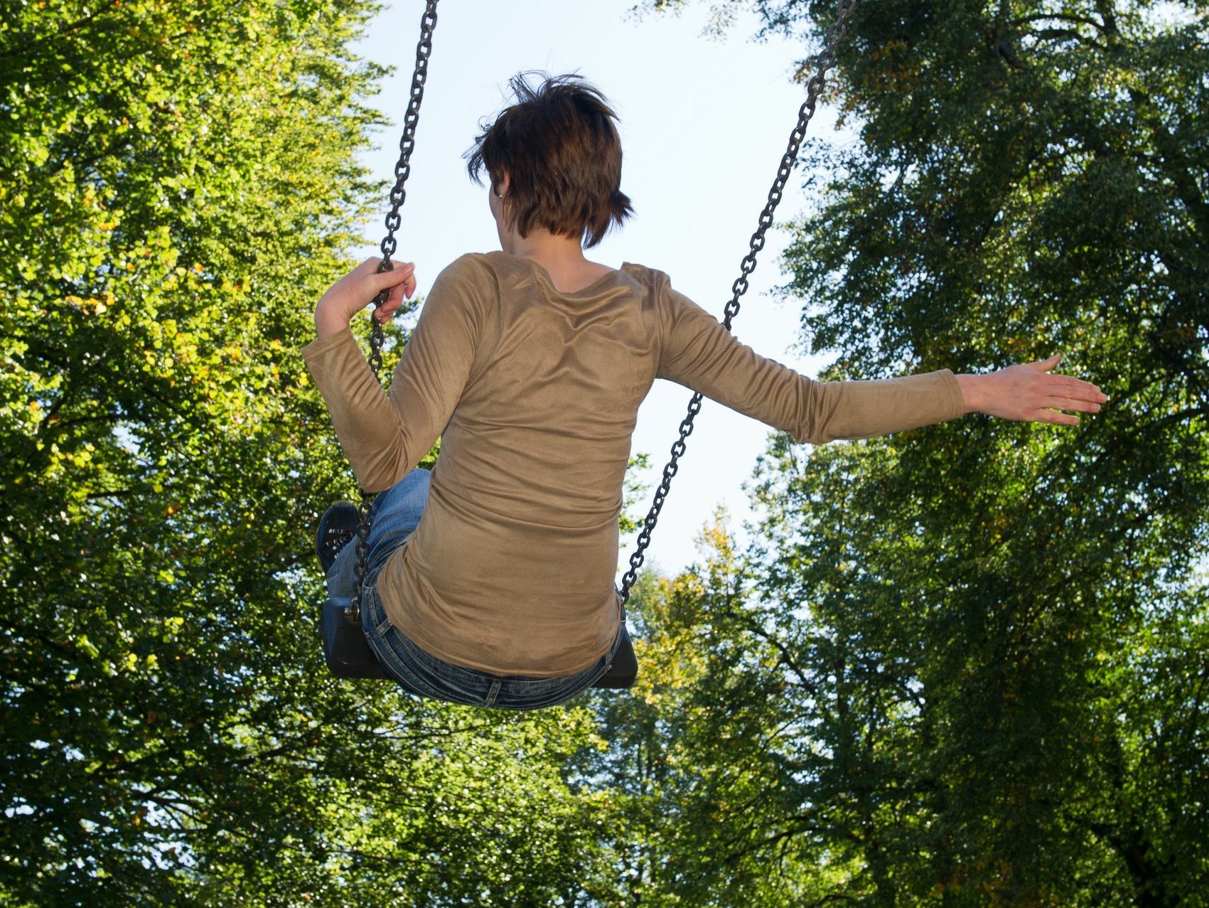 Im Garten: eine Frau schaukelt hoch hinaus. Dabei hält sie sich nur mit einer Hand an der Schaukelkette fest