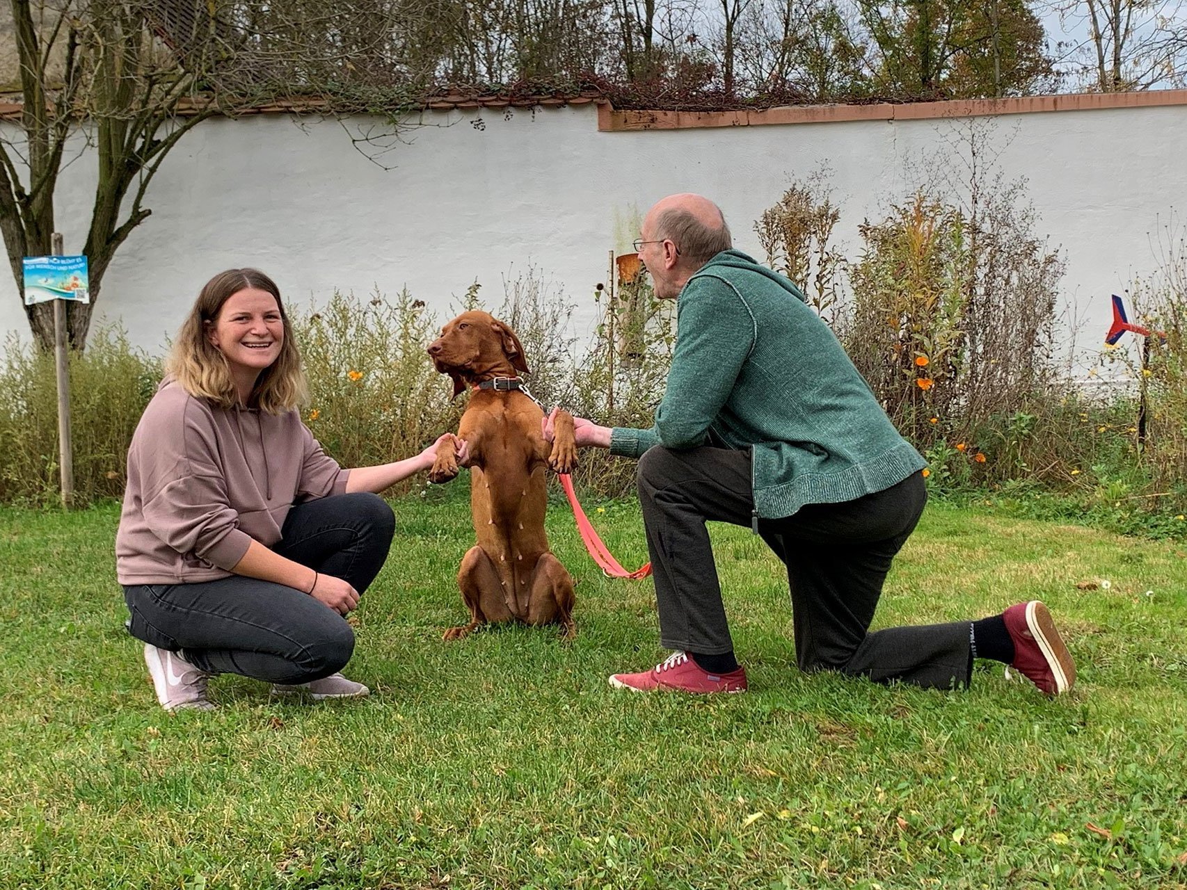 eine Frau und ein Mann spielen mit einem Hund im Garten