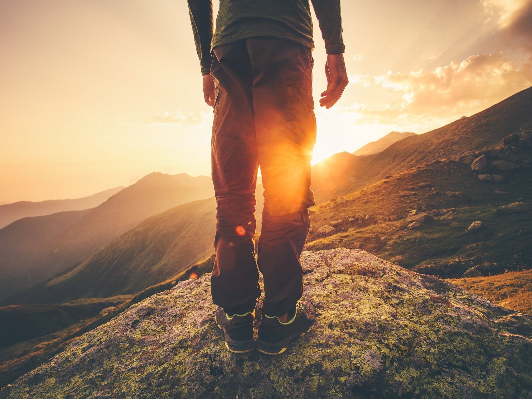 Symbolbild: ein Mann im Trekking-Outfit steht auf einem Berg - Die Sonne geht auf