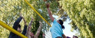 Action: eine Gruppe Frauen und Männer spielen Volleyball - eine Frau "lupft" gerade den Ball über den "Block"